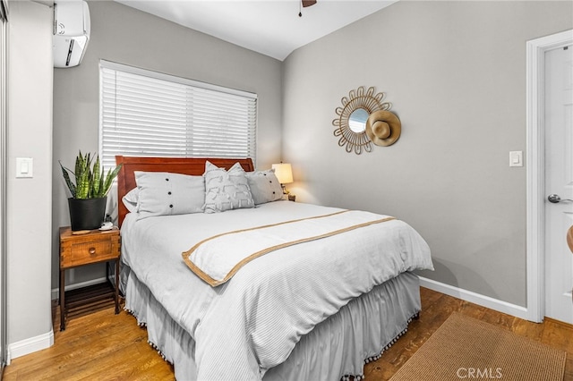 bedroom featuring a wall mounted air conditioner, wood-type flooring, and ceiling fan