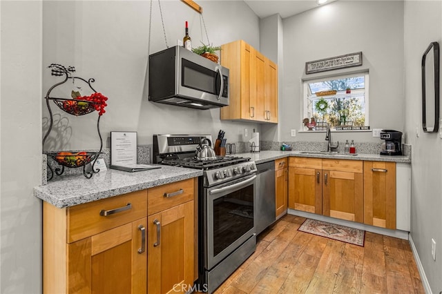 kitchen with stainless steel appliances, light stone countertops, sink, and light hardwood / wood-style flooring