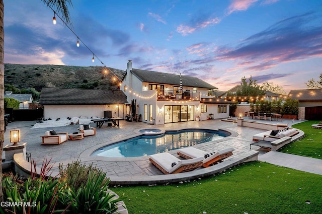 pool at dusk featuring an in ground hot tub and a patio