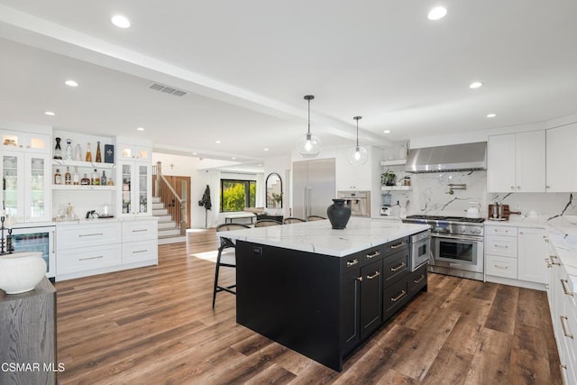 kitchen with premium appliances, a large island, decorative backsplash, wall chimney exhaust hood, and white cabinets