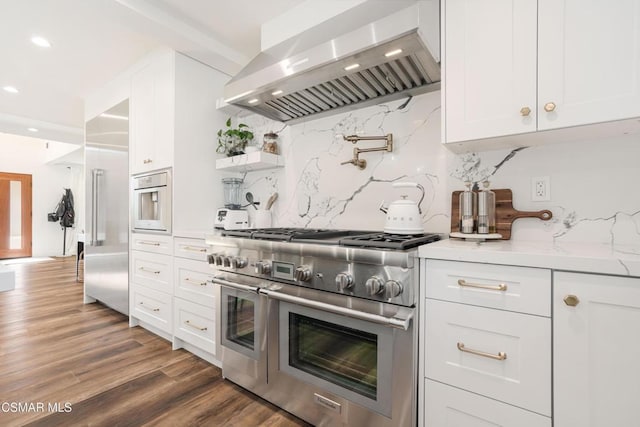 kitchen featuring double oven range, ventilation hood, backsplash, white cabinets, and light stone counters