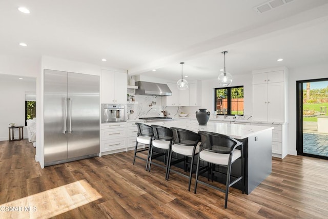 kitchen with appliances with stainless steel finishes, white cabinetry, and wall chimney range hood