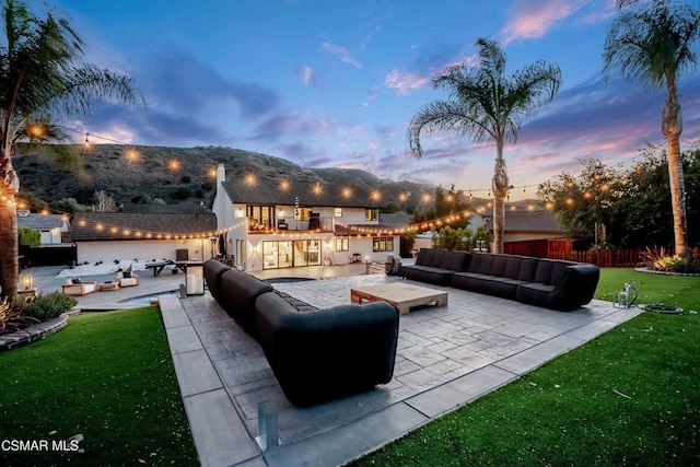 patio terrace at dusk featuring outdoor lounge area, a lawn, and exterior bar