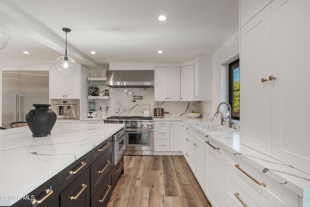 kitchen with white cabinets, wall chimney exhaust hood, decorative light fixtures, stainless steel appliances, and tasteful backsplash