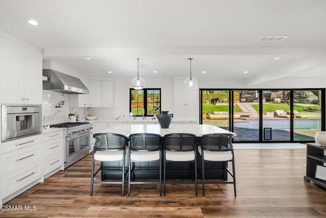 kitchen with white cabinetry, wall chimney range hood, stainless steel appliances, and a kitchen island