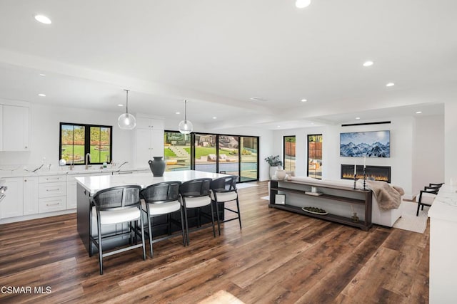 kitchen with pendant lighting, white cabinets, dark hardwood / wood-style flooring, an island with sink, and a breakfast bar