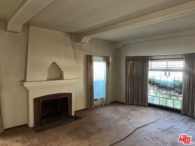 unfurnished living room featuring beamed ceiling, carpet, and a fireplace