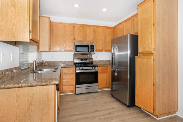 kitchen with appliances with stainless steel finishes, sink, stone countertops, and light hardwood / wood-style flooring