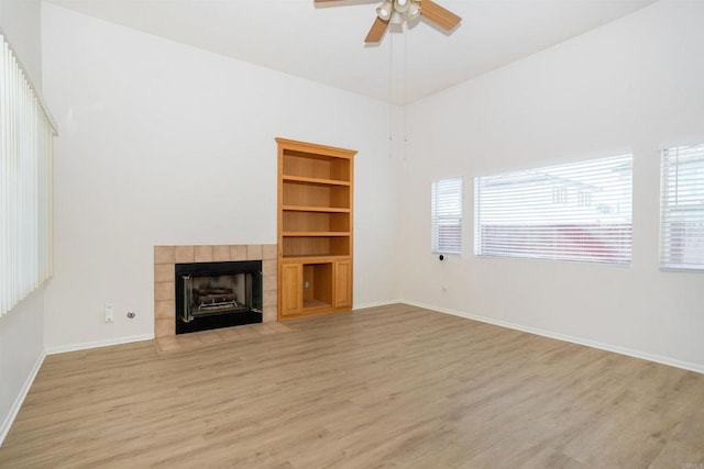 unfurnished living room featuring ceiling fan, a tiled fireplace, built in features, and plenty of natural light