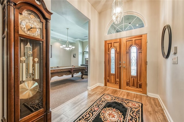 entrance foyer featuring a high ceiling, a notable chandelier, crown molding, hardwood / wood-style floors, and pool table