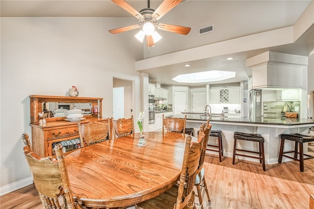 dining area featuring a skylight, ceiling fan, sink, a high ceiling, and light hardwood / wood-style flooring