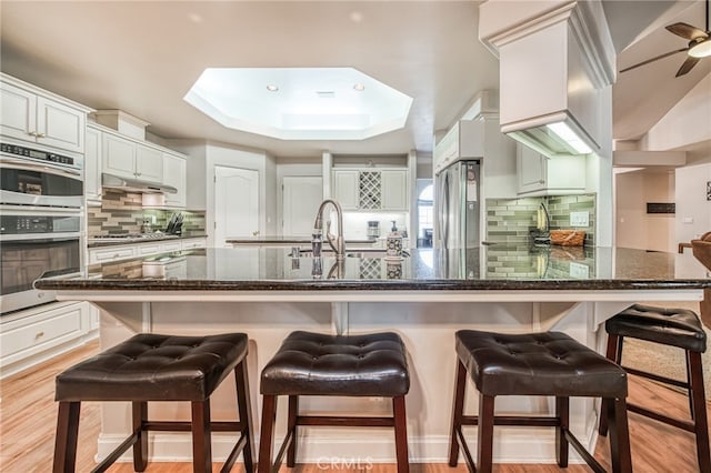 kitchen with white cabinets, light hardwood / wood-style floors, a breakfast bar area, and appliances with stainless steel finishes