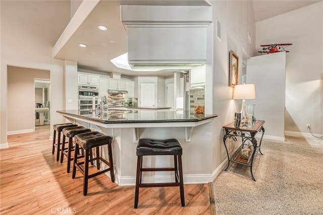 kitchen with a kitchen breakfast bar, backsplash, kitchen peninsula, double oven, and white cabinets