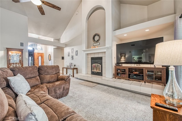 carpeted living room with ceiling fan, a tile fireplace, and high vaulted ceiling