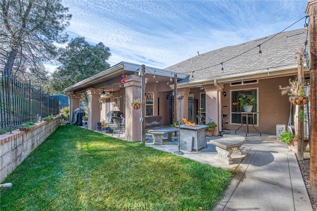 rear view of property featuring ceiling fan, a yard, a patio, and an outdoor fire pit