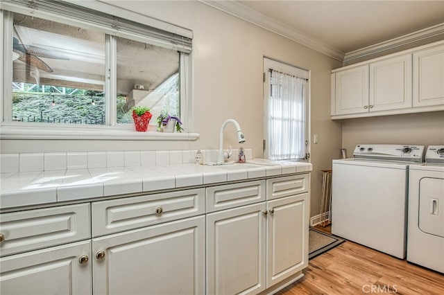 laundry area featuring cabinets, crown molding, sink, washer and dryer, and light hardwood / wood-style floors