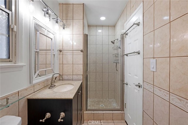 bathroom with tile patterned flooring, toilet, walk in shower, vanity, and tile walls