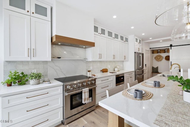 kitchen featuring backsplash, a barn door, appliances with stainless steel finishes, white cabinetry, and a sink