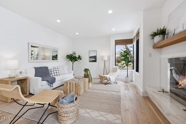 living area with a glass covered fireplace, recessed lighting, light wood-type flooring, and baseboards