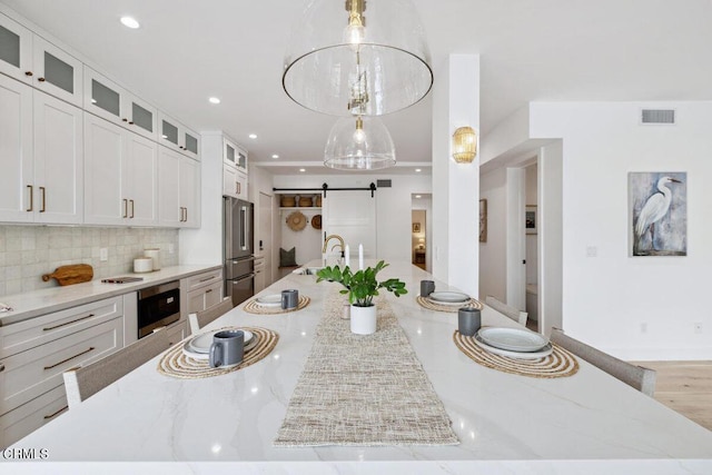 kitchen with visible vents, a spacious island, a barn door, stainless steel appliances, and decorative backsplash