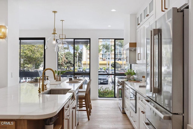 kitchen with an island with sink, light wood-type flooring, light stone counters, appliances with stainless steel finishes, and a sink