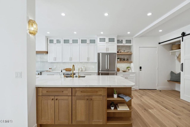 kitchen with open shelves, light wood-style flooring, freestanding refrigerator, a sink, and a barn door