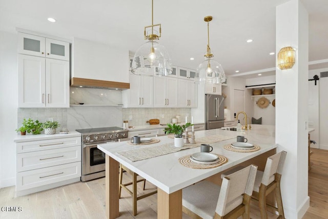 kitchen featuring premium range hood, light wood-type flooring, high quality appliances, a sink, and a barn door