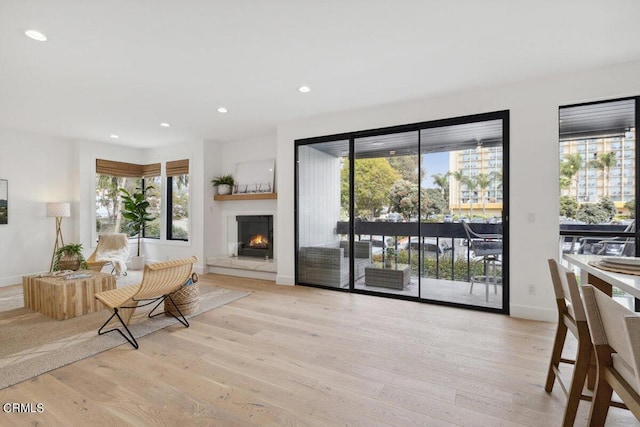 living room featuring recessed lighting, baseboards, light wood-type flooring, and a lit fireplace