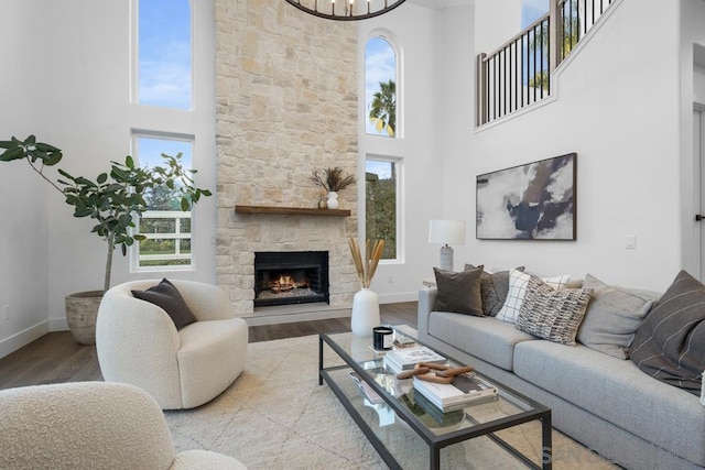 living room featuring an inviting chandelier, light hardwood / wood-style floors, a towering ceiling, and a stone fireplace