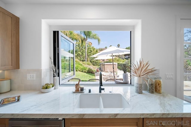 kitchen with light stone counters, sink, backsplash, and stainless steel dishwasher