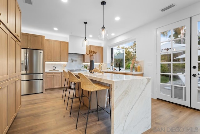 kitchen featuring stainless steel fridge with ice dispenser, tasteful backsplash, hanging light fixtures, a kitchen island, and light hardwood / wood-style flooring