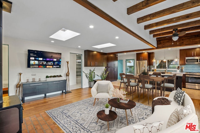 living room with ceiling fan, a skylight, and beamed ceiling