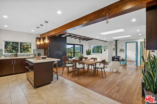 kitchen featuring a kitchen island, beamed ceiling, dark brown cabinetry, hanging light fixtures, and a wood stove