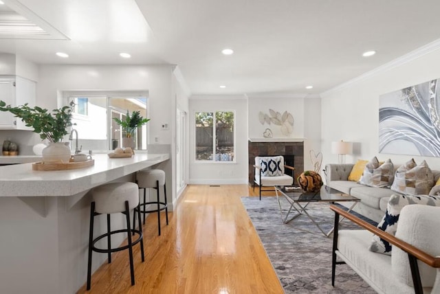 living room with a tiled fireplace, crown molding, sink, and light hardwood / wood-style flooring