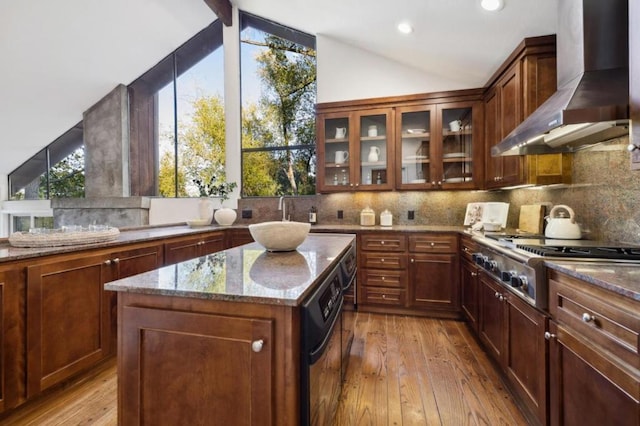 kitchen featuring a center island, stainless steel gas cooktop, light stone countertops, wall chimney range hood, and light hardwood / wood-style flooring