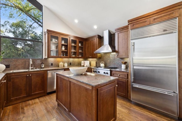 kitchen with wall chimney exhaust hood, lofted ceiling, sink, a center island, and stainless steel appliances