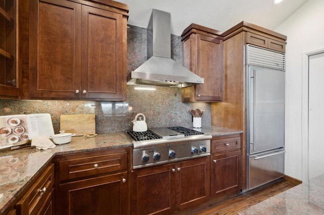 kitchen with stainless steel appliances, tasteful backsplash, light stone countertops, vaulted ceiling, and wall chimney exhaust hood