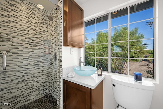 bathroom with toilet, vanity, a healthy amount of sunlight, and tiled shower