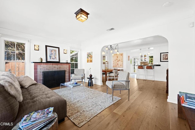 living room with plenty of natural light, hardwood / wood-style flooring, a chandelier, and a brick fireplace