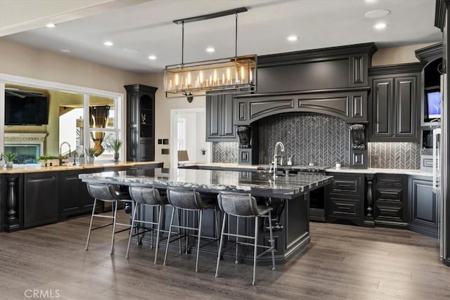 kitchen with a breakfast bar, decorative backsplash, dark wood-type flooring, and a center island with sink