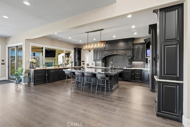 kitchen featuring decorative light fixtures, a center island with sink, decorative backsplash, light hardwood / wood-style flooring, and a breakfast bar area