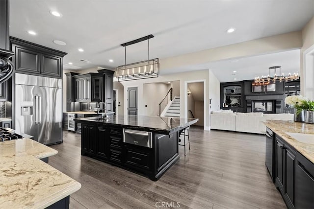 kitchen with stainless steel built in refrigerator, a spacious island, a kitchen breakfast bar, hanging light fixtures, and light stone counters