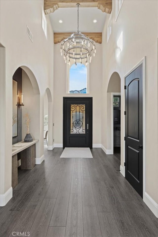 foyer entrance featuring a towering ceiling, beamed ceiling, an inviting chandelier, and dark hardwood / wood-style floors