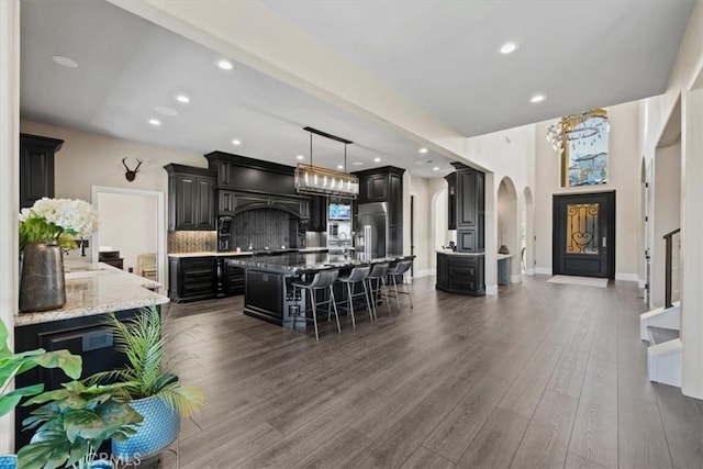 kitchen with premium range hood, an island with sink, tasteful backsplash, high end refrigerator, and dark wood-type flooring