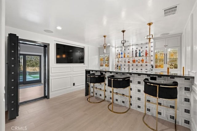 bar with white cabinets, light hardwood / wood-style floors, and pendant lighting