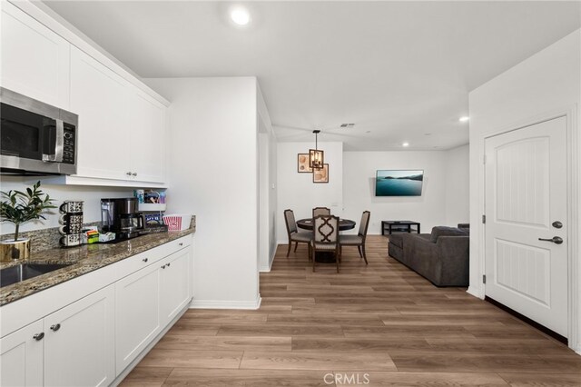 kitchen with hanging light fixtures, white cabinets, dark stone counters, and light wood-type flooring