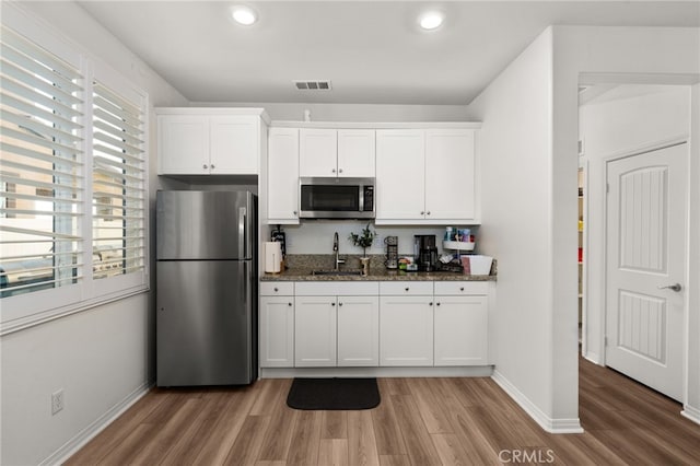 kitchen featuring appliances with stainless steel finishes, sink, dark stone countertops, and white cabinetry