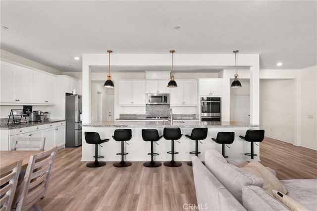 kitchen with hanging light fixtures, white cabinets, a kitchen island with sink, and stainless steel appliances