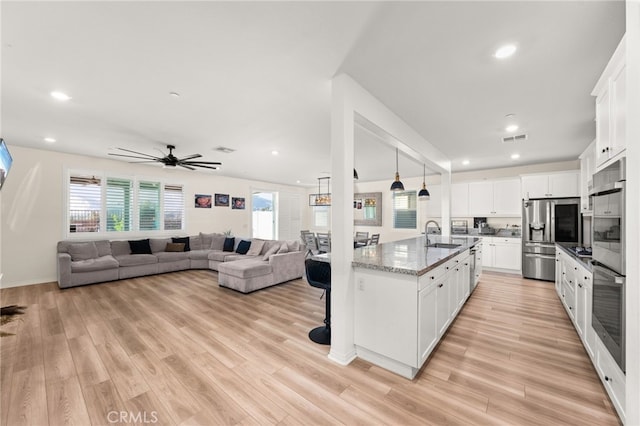 kitchen featuring a center island with sink, appliances with stainless steel finishes, dark stone countertops, white cabinets, and sink