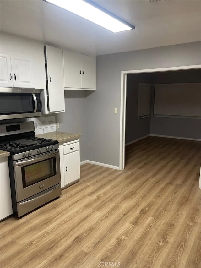 kitchen with light stone countertops, white cabinets, appliances with stainless steel finishes, and light hardwood / wood-style flooring